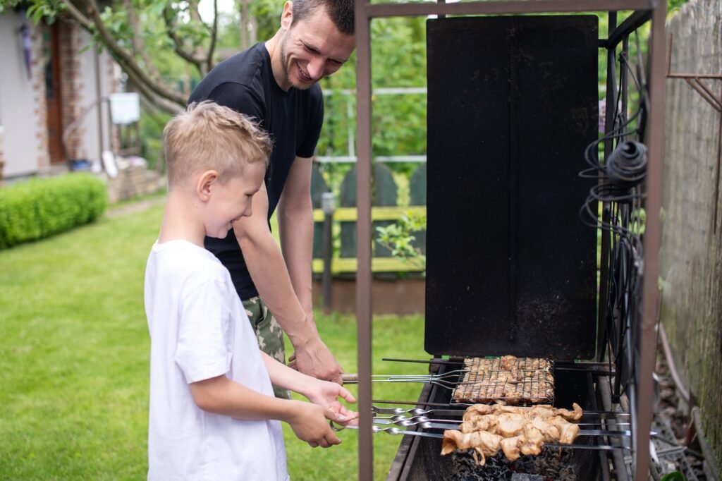 cheerful-dad-and-son-roast-meat-on-the-grill-2023-11-27-05-29-21-utc