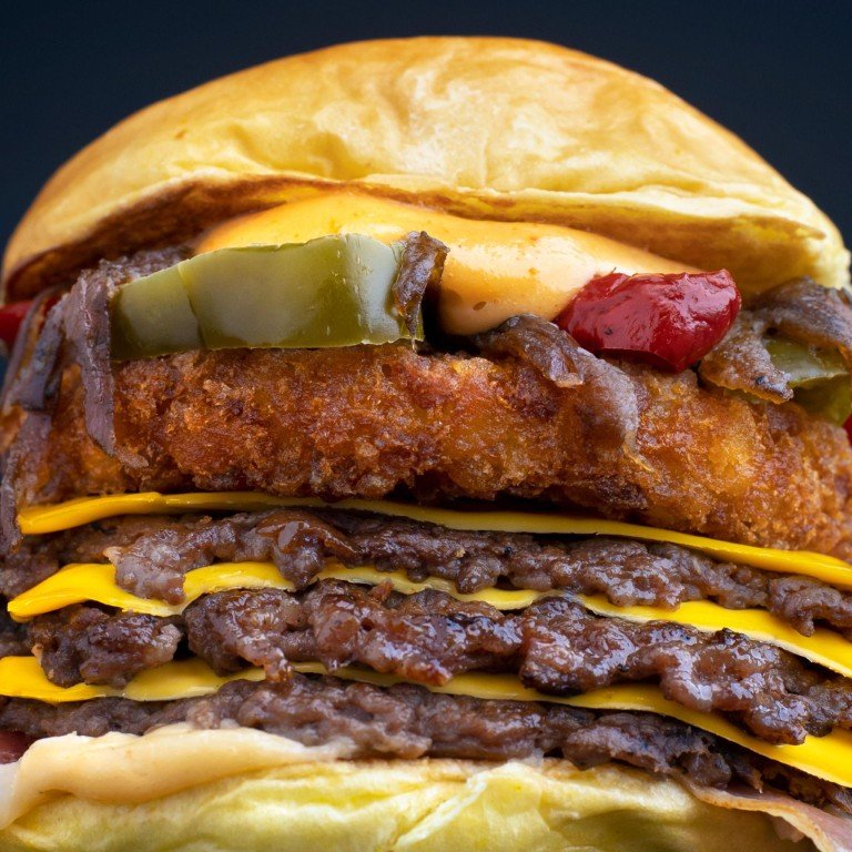 Close-up of a tall cheeseburger with a crispy fried patty, melted cheddar, pickles, onions, and a soft bun.