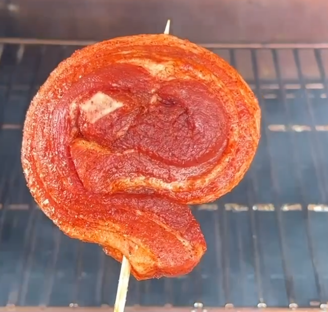 Pinwheels 6 Spiral-cut grilled meat skewered on a stick over a barbecue grill, with charred edges around the roll.