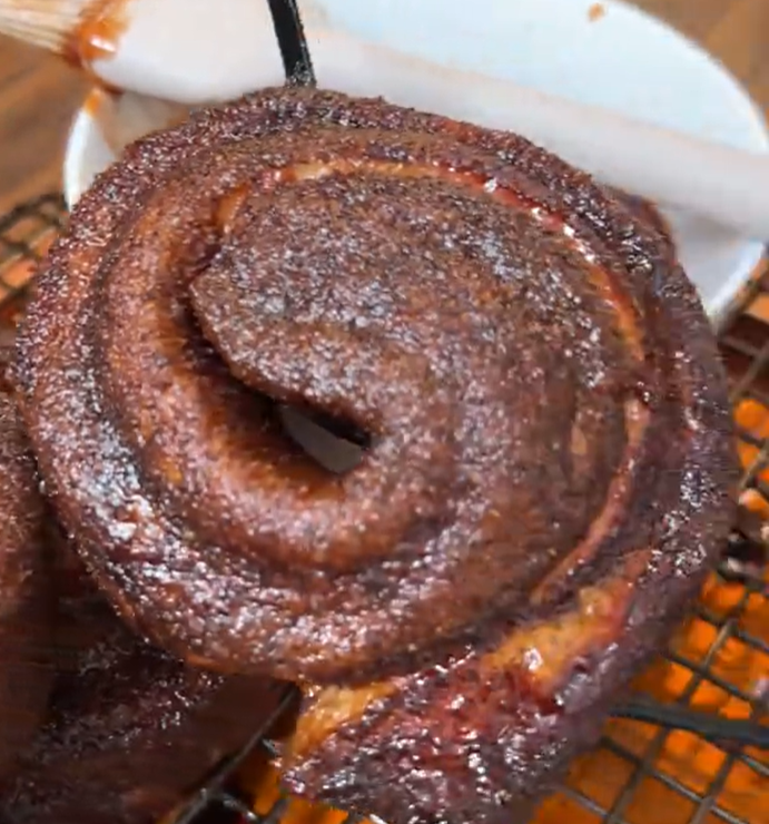Screenshot 2026-05-29 104826 Close-up of a glossy, spiraled cinnamon roll with a caramel glaze on a plate.