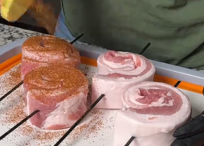 Screenshot 2026-05-29 104939 Uncooked pork loin rounds on a metal grill rack, coated with a brown spice rub and pepper.