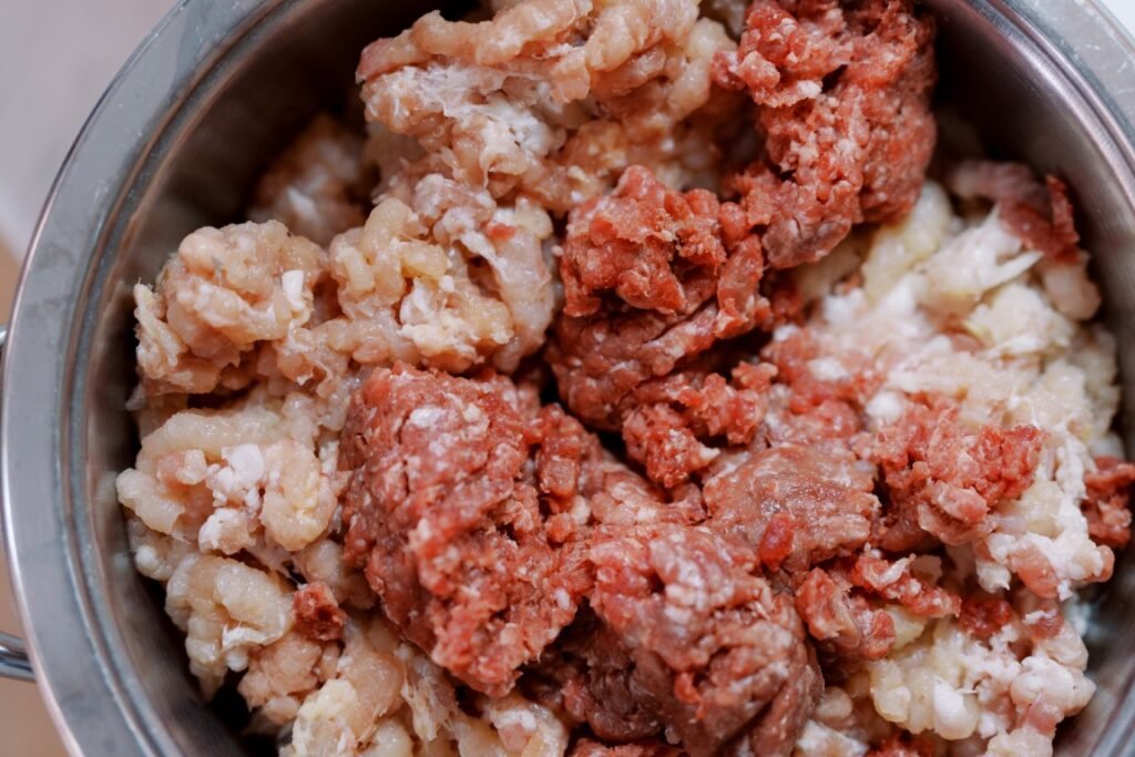 Raw ground meat mixture (beef and pork) in a stainless steel pot, ready to be seasoned.