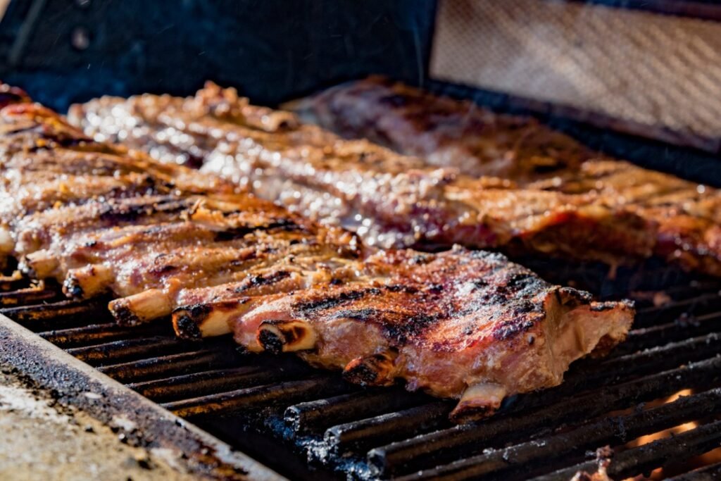 delicious-ribs-cooking-on-the-grill-closeup-shot-2026-03-16-04-26-45-utc Pork ribs cooking on a charcoal grill with sizzling juices and charred edges over open flames