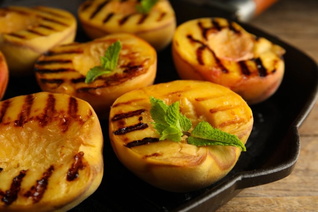 Delicious grilled peaches with mint on table closeup Grilled peach halves with mint leaves on a cast-iron skillet, showing caramelized grill marks.