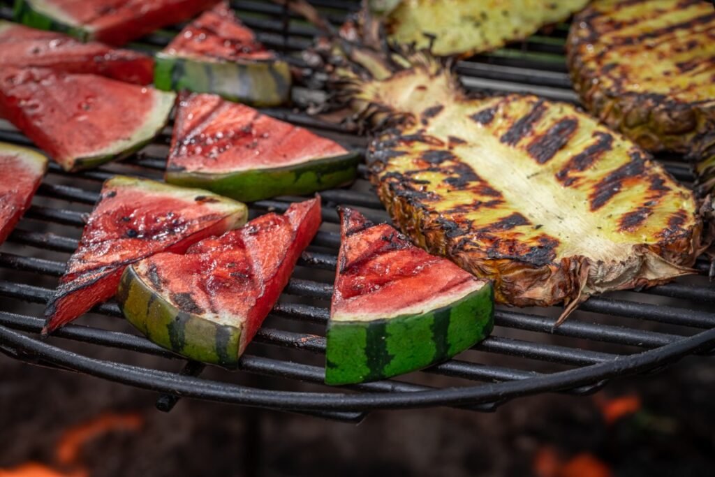 Sweet sear watermelon and pineapple with herbs and spices Watermelon wedges grilling on a barbecue with pineapple slices in the background.