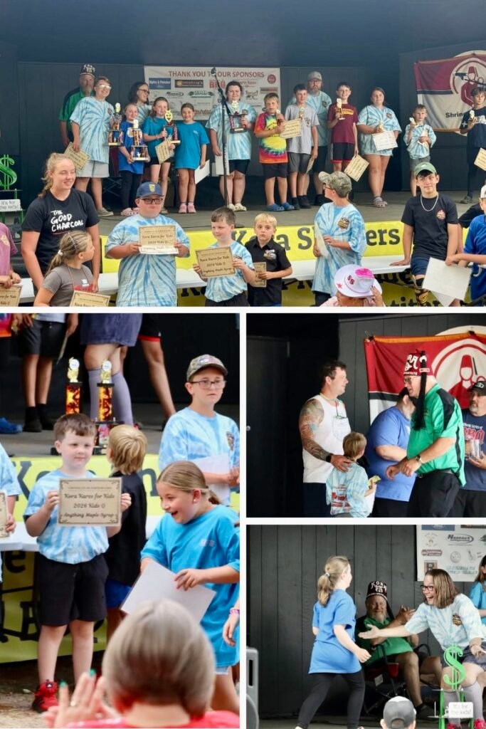 Group of children on a stage receiving trophies and certificates at an awards ceremony with banners in the background.
