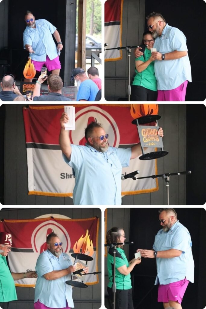Bearded man in a light blue shirt and pink shorts holds a flaming trophy on stage as the audience watches.
